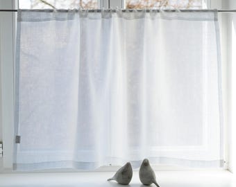 May include: Sheer white curtain panel with a gray border, hanging from a metal rod in a window. Two small, gray bird figurines sit on the windowsill below the curtain. The curtain allows light to filter through.