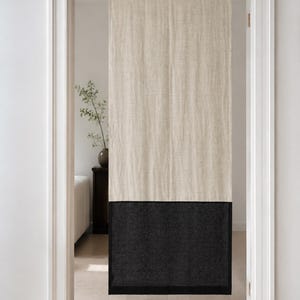 Puede incluir: Una cortina de puerta de lino de dos tonos. La secci&oacute;n superior es de color beige natural y la inferior es gris carb&oacute;n oscuro. La cortina cuelga en una puerta con molduras blancas y un suelo de madera clara.