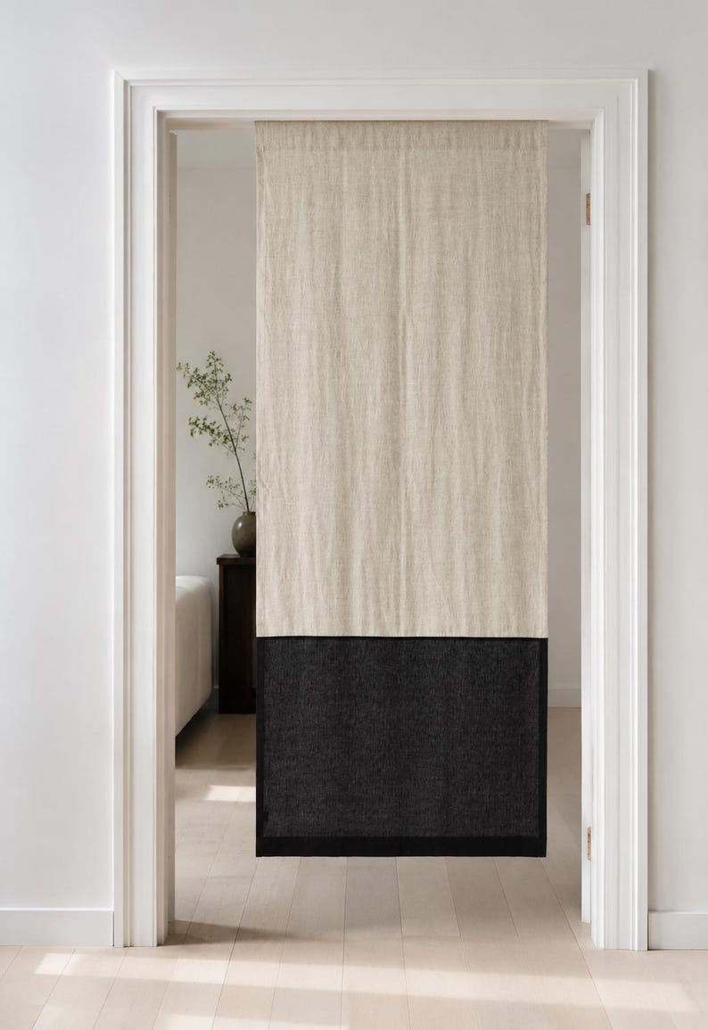 Puede incluir: Una cortina de puerta de lino de dos tonos. La secci&oacute;n superior es de color beige natural y la inferior es gris carb&oacute;n oscuro. La cortina cuelga en una puerta con molduras blancas y un suelo de madera clara.