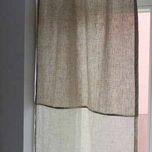 May include: A linen window curtain in shades of beige and off-white. The curtain is divided into two sections, with a darker beige border framing the bottom and top. The fabric has a textured appearance, and it hangs from a rod above a window.