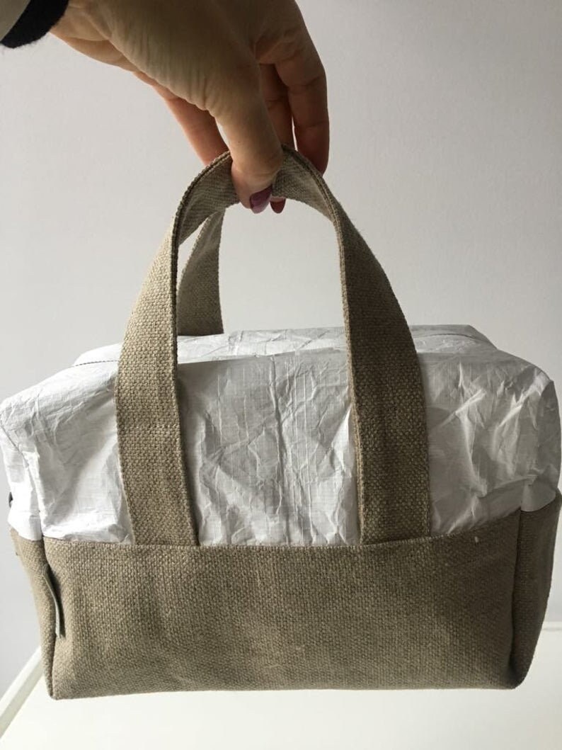 May include: A small, beige canvas tote bag with a white paper lining and two thick canvas handles.