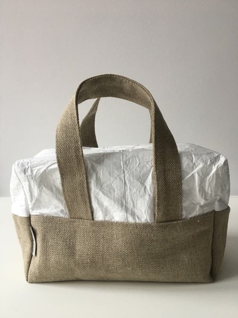May include: A beige linen tote bag with a white paper lining. The bag has two handles and a rectangular shape.