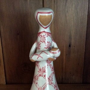May include: White ceramic figurine of a woman holding a baby. The figurine is decorated with a pink and white floral pattern.