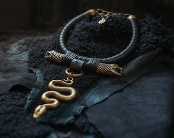 May include: A black leather choker necklace with two gold snake head accents. A gold snake pendant hangs from the choker.
