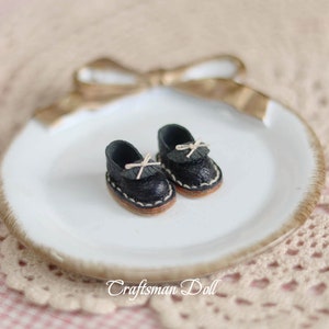 May include: A pair of black leather doll shoes with white laces and a bow on each shoe. The shoes are sitting on a white plate with a gold rim.