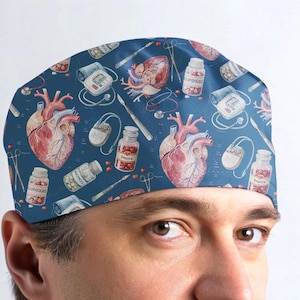 May include: A blue scrub cap featuring a repeating medical pattern of anatomical hearts, pill bottles labeled Digoxin and Clopidogrel, surgical scalpels, stethoscopes, and blood pressure monitors. The design is printed across the fabric surface.