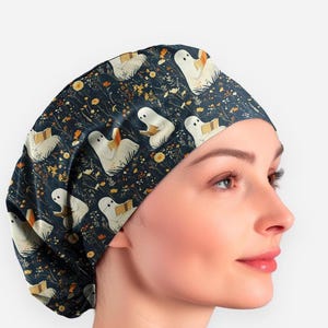 May include: A dark blue surgical scrub cap featuring a repeating pattern of cartoon ghosts reading books, with yellow and orange floral accents. The cap is made of a soft, flexible material.