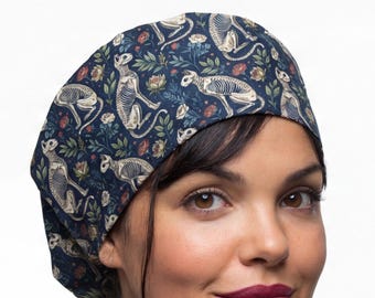 Peut inclure: Une charlotte de bloc bleu foncé ornée d'un motif répétitif de squelettes de chats blancs entremêlés de petites fleurs rouges, de feuilles vertes et de fleurs blanches. Le tissu présente une coupe ajustée couvrant le haut de la tête.