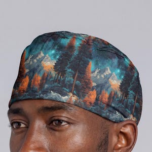 May include: A patterned cap featuring a mountain and forest design. The cap's fabric displays a night sky with stars, pine trees, and mountain peaks in shades of teal, orange, and white. The cap is worn on a person's head.