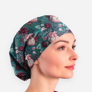 May include: A teal surgical scrub cap featuring a floral pattern with anatomical heart illustrations and roses. The cap is designed to cover the head and hair, commonly used in medical settings. The design includes pink, burgundy, and white floral elements.
