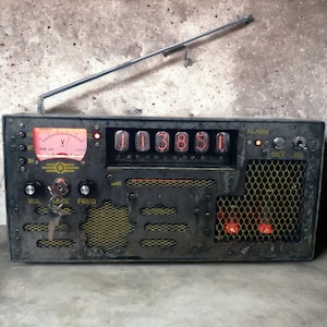 May include: A vintage-style radio with a dark gray, industrial design. It features a digital display, a tuning dial, and a speaker grill. The radio has a retro aesthetic with a metallic antenna and a glowing meter.