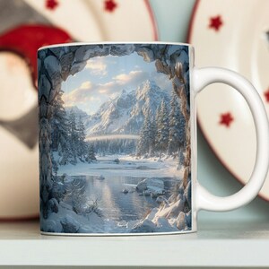 May include: White ceramic mug with a winter scene printed on it. The scene shows a snowy mountain range with a frozen lake in the foreground. The image is framed by a stone archway.