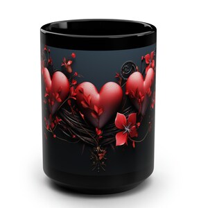 May include: Black coffee mug with a design of three red hearts surrounded by red flowers and vines on a dark blue background.