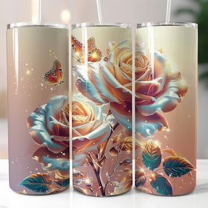 Könnte beinhalten: Drei Edelstahlbecher mit floralem Design. Die Becher haben einen hellrosa Hintergrund mit einer großen Rose in Blautönen, Rosa und Gelb. Die Rosen sind von grünen Blättern und zwei Schmetterlingen umgeben.