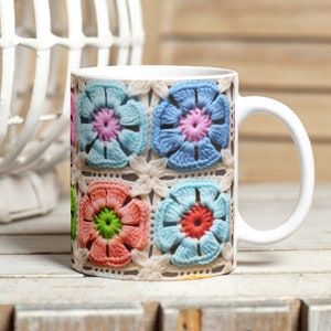 Puede incluir: Taza de cerámica blanca con un diseño de flores de ganchillo de colores. Las flores son en tonos de rosa, azul, verde y naranja.