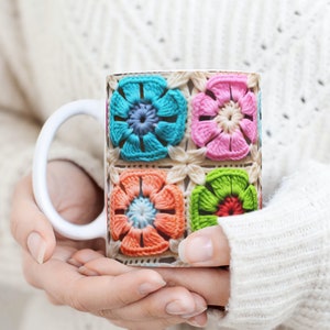 Puede incluir: Taza de cer&aacute;mica blanca con un dise&ntilde;o de ganchillo colorido con flores rosas, azules, verdes y naranjas.