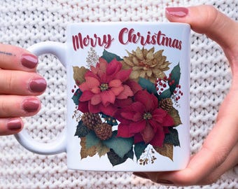 Może przedstawiać: Biały ceramiczny kubek z napisem "Merry Christmas" w czerwonym skrypcie. Kubek ma kwiatowy wzór z czerwonymi gwiazdami betlejemskimi, złotymi kwiatami, szyszkami i jagodami, idealny na święta.