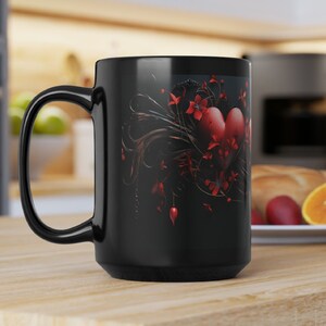 May include: Black ceramic coffee mug with a red heart and floral design. The heart is surrounded by black vines and red flowers.