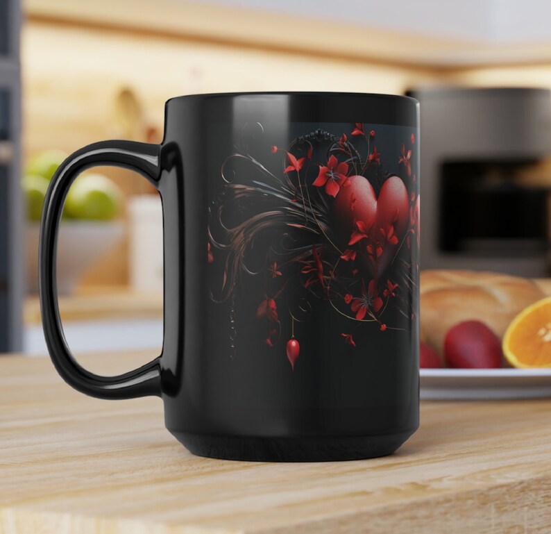 May include: Black ceramic coffee mug with a red heart and floral design. The heart is surrounded by black vines and red flowers.