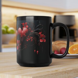 May include: Black ceramic coffee mug with a red heart and floral design. The design features a large red heart with intricate black swirls and red flowers.