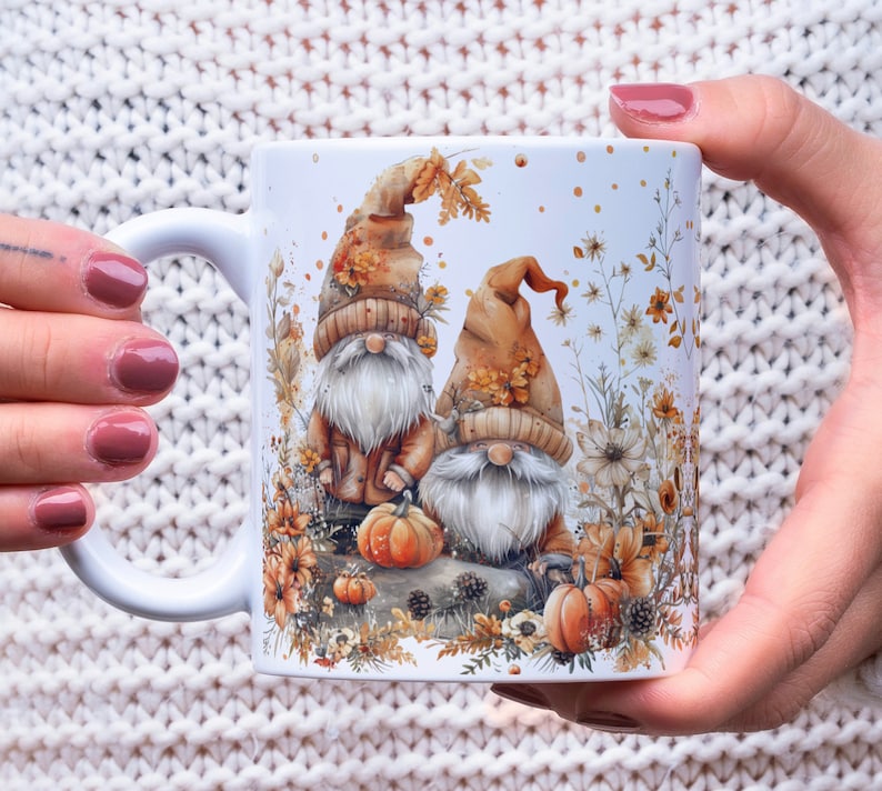 May include: White ceramic mug with a fall-themed design featuring two gnomes with orange and brown hats, surrounded by autumn leaves, pumpkins, and flowers.