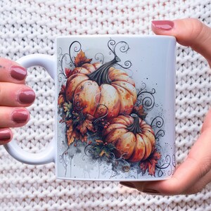 May include: White ceramic mug with a watercolor design of two orange pumpkins with green vines and leaves. The pumpkins are surrounded by a swirling pattern of vines and leaves.