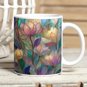 Può includere: Tazza in ceramica bianca con un colorato motivo floreale. Il design presenta fiori stilizzati nei toni del rosa, viola, giallo e verde, con un effetto vetrata. La tazza ha un manico bianco e una finitura lucida. Altezza: circa 9,5 cm.