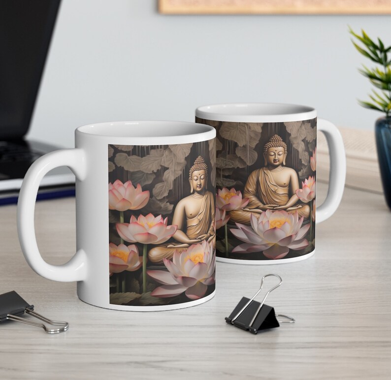 May include: Two white ceramic mugs with a design of two golden Buddhas meditating on lotus flowers. The background is a dark brown with a pattern of leaves.