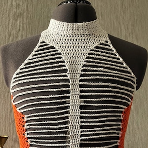 May include: A handmade crochet halter top in white, orange, and black. The top features a high neckline and a unique design with horizontal white stripes and orange side panels. The garment is displayed on a mannequin.