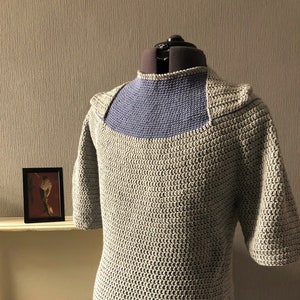 May include: A crocheted top with short sleeves in a light grey colour with a blue trim around the neck and bottom hem.