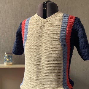 以下が含まれることがあります： Vネックとブルー、レッド、ネイビーブルーの縦縞が入ったベージュのクロシェ編み半袖シャツ