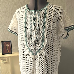 May include: A white crochet top featuring a lace-up front with white ribbon ties. The garment has a mesh pattern throughout, accented by vertical panels of dark gray and teal geometric stitching along the chest and sleeve edges.