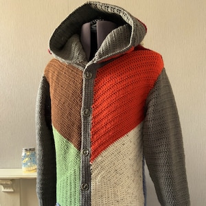Peut inclure: Un cardigan à capuche avec un motif géométrique dans les tons de gris, marron, vert, orange et bleu. Le cardigan a une fermeture boutonnée et une poche sur le devant.