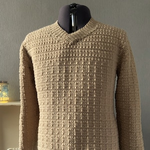 May include: A beige crocheted sweater with a v-neck.