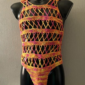 May include: A crocheted garment with a geometric pattern in shades of pink and yellow. The garment is sleeveless and has a low neckline. It is made of a lightweight, breathable material.
