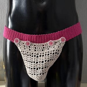 May include: A crocheted undergarment with a pink waistband and beige crocheted mesh. The waistband has four pink flowers with white centers.