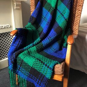 May include: A blue, green and black striped crocheted throw blanket with fringe on the edges. The blanket is draped over a wooden chair.