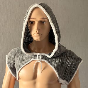 May include: A grey crocheted hooded top with white trim. The top is sleeveless and has a tie at the front.