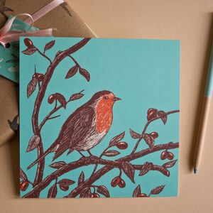 May include: A teal blue greeting card with a robin perched on a branch with red berries. The robin is illustrated in brown and red with a white breast.