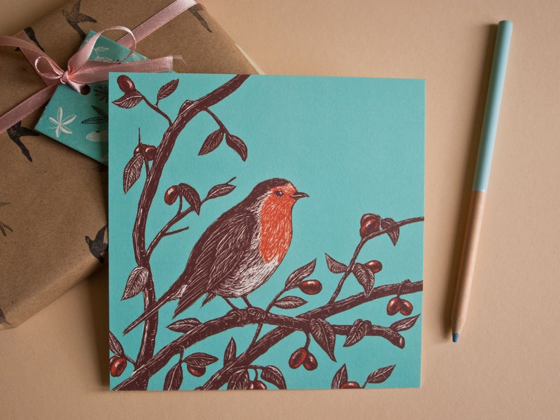 May include: A teal blue greeting card with a robin perched on a branch with red berries. The robin is illustrated in brown and red with a white breast.