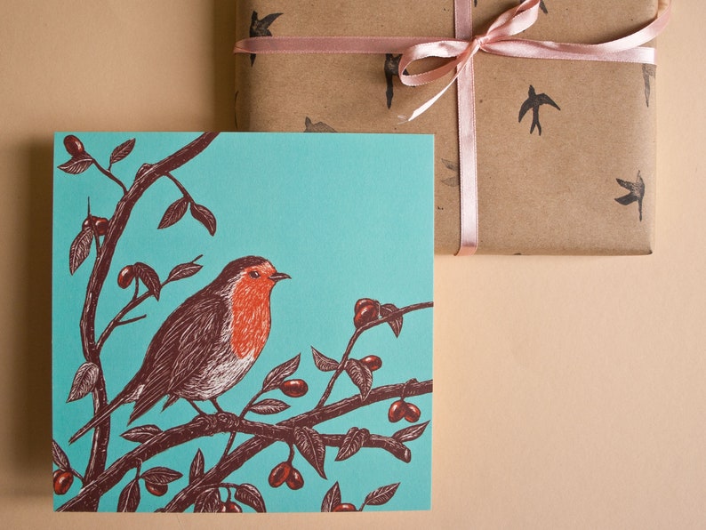 May include: A turquoise blue greeting card with a robin perched on a branch with red berries. The robin is brown and white with a red breast.