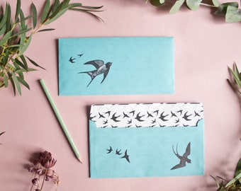 May include: Two light blue envelopes featuring a black swallow design. The smaller envelope has a single swallow in flight, while the larger envelope has a repeating pattern of swallows.