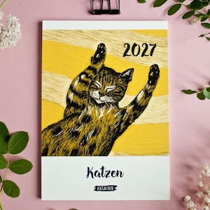 May include: A 2027 wall calendar featuring a black and brown tabby cat stretching on a yellow background with white horizontal stripes. The text "2027" appears in the upper right, while the word "Katzen" and "KATJA RUB" are printed at the bottom.