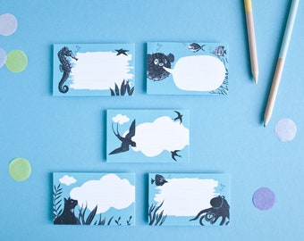 May include: Set of five blue notepads featuring various sea creature illustrations. Each notepad has a white space for writing notes. The illustrations include a seahorse, a pufferfish, a swallow, a cat, and an octopus.