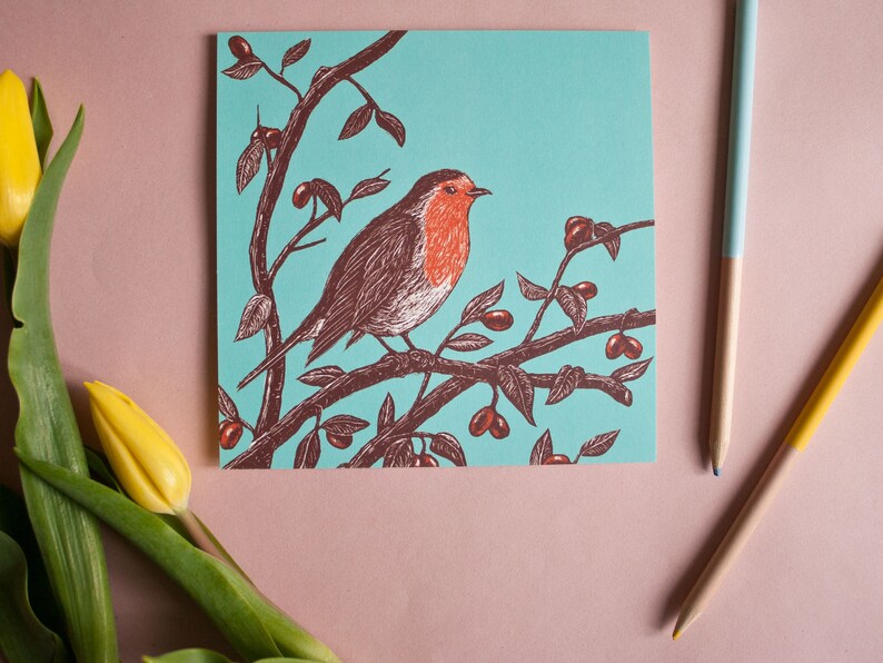 May include: A greeting card with a robin perched on a branch with red berries. The robin is brown with a red breast and is set against a turquoise background.