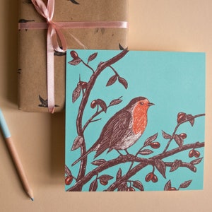May include: A robin perched on a branch with red berries, against a turquoise background. The robin has a red breast and brown wings. The illustration is in a vintage style.