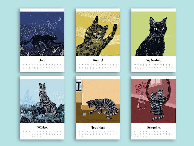 May include: A wall calendar featuring six monthly pages from July to December, each displaying a unique illustration of a cat in various settings, including outdoor scenes, indoor play, and mirror reflections, with printed month names and dates.