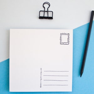 May include: A blank white postcard with a black stamp outline and lines for an address. A black pencil and a black binder clip are on a blue and white background.