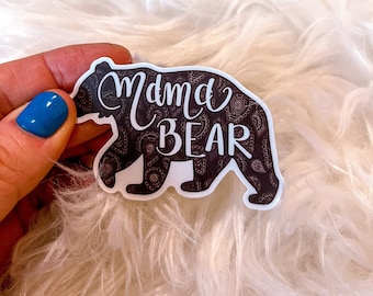 May include: A black bear silhouette sticker with a white paisley pattern and the text "Mama Bear" in white lettering.