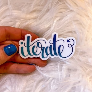May include: A white sticker with the word "iterate" written in blue and teal cursive lettering with a small arrow at the end of the word.